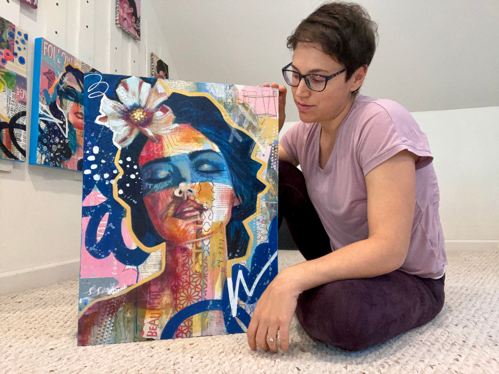 artist sitting on the floor with a colorful art piece featuring a face and abstract elements.
